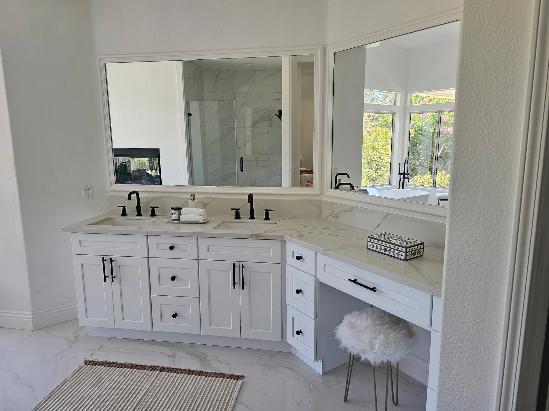 Long white bathroom vanity with two sinks, large mirrors and dark faucets.