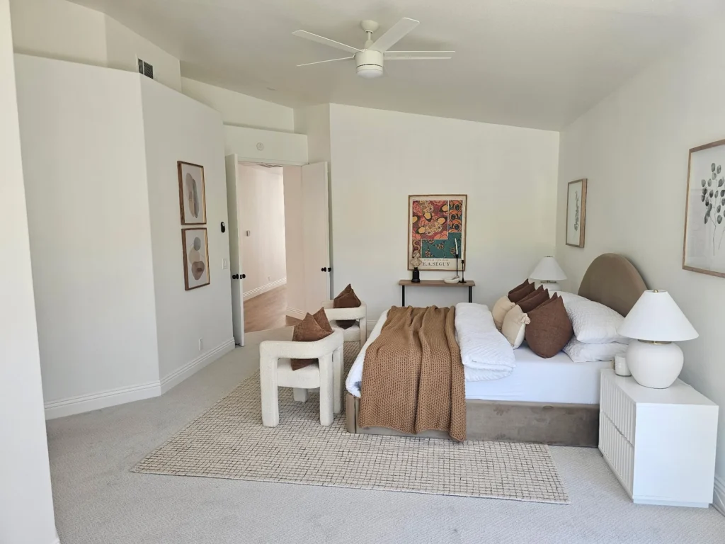 Bedroom with light walls, a ceiling fan and wood flooring around a neutral area rug.