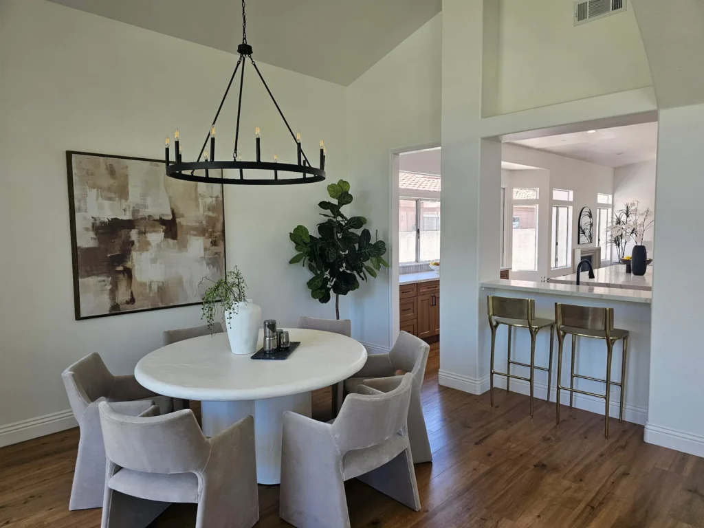 Round dining table beneath a black chandelier, with an open view into the kitchen.